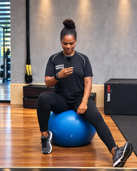 Patrícia sentada na bola suíça azul em uma academia