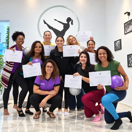 Turma do curso de Pilates Solo reunida com os certificados e bolas de Pilates em frente ao logo do estúdio